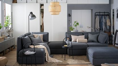 A grey modular sofa setup in a small apartment with coat rack storage in background