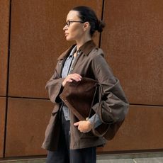 Woman wears brown barn jacket, grey cardigan, black jeans and carries a brown suede bag