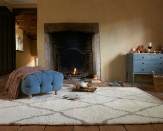 Cozy period living room with fireplace, lit fire, berber cream rug, blue ottoman, blue cabinet, candles, tray with teapot