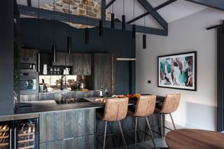Dark brown wood panelled kitchen and breakfast bar with brown leather bar stools and black pendant lights overhead