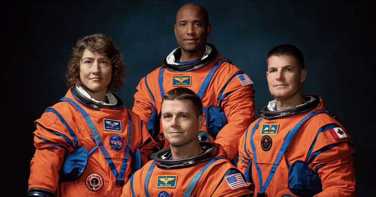 four astronauts standing in spacesuits against a dark background