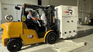 a yellow forklift carries a large white box with the words &quot;rocket lab&quot; on its side