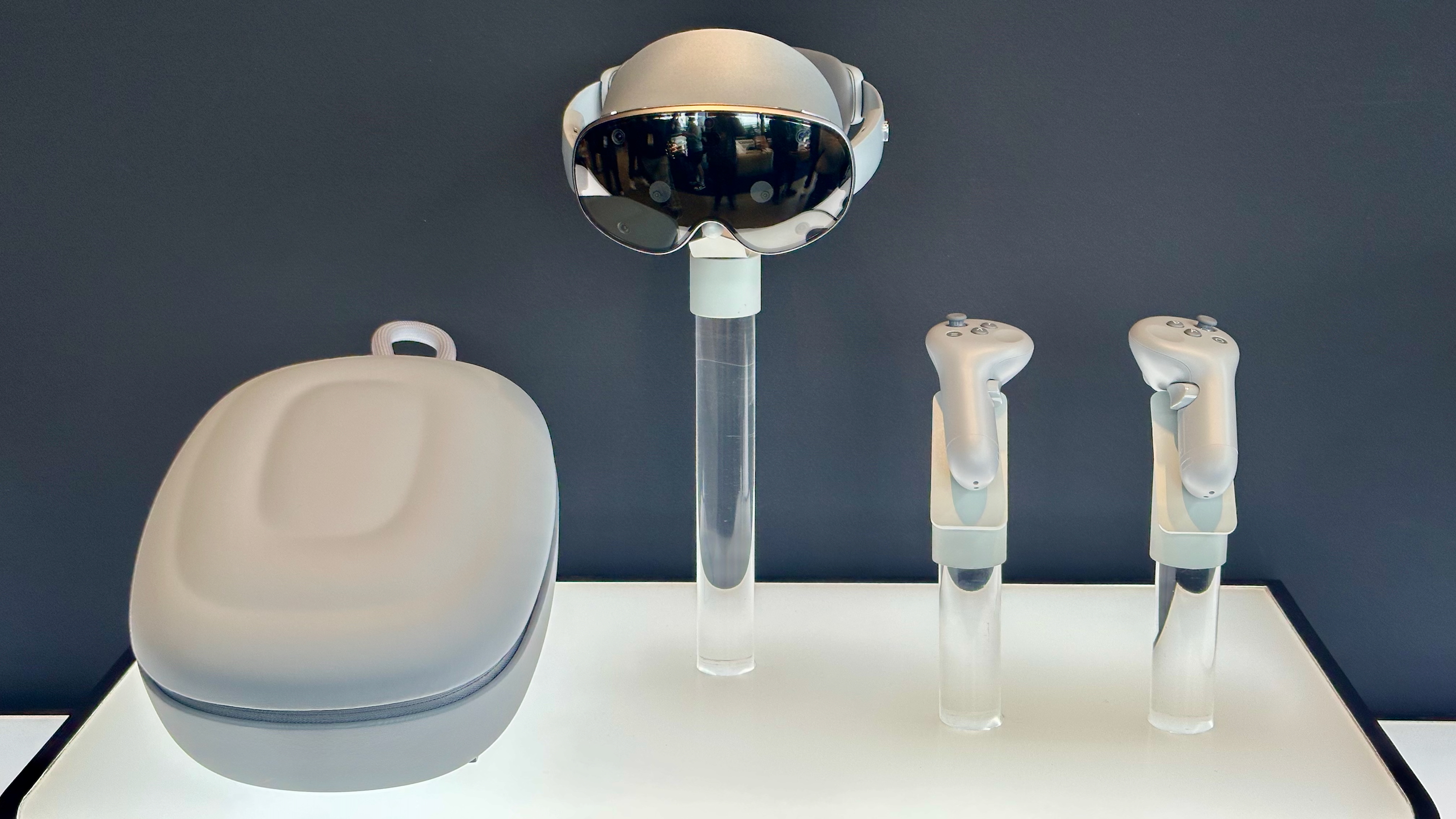 A photo of the Samsung Galaxy XR headset, carrying case, and controllers sitting on four separate plastic pedestals.