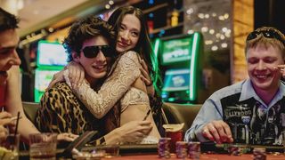 mikey madison as anora and as she embraces ivan played by Mark Eidelstein sitting at a blackjack table in a casino