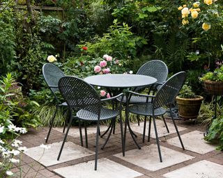 A small paved area with outdoor dining table and lush surround planting