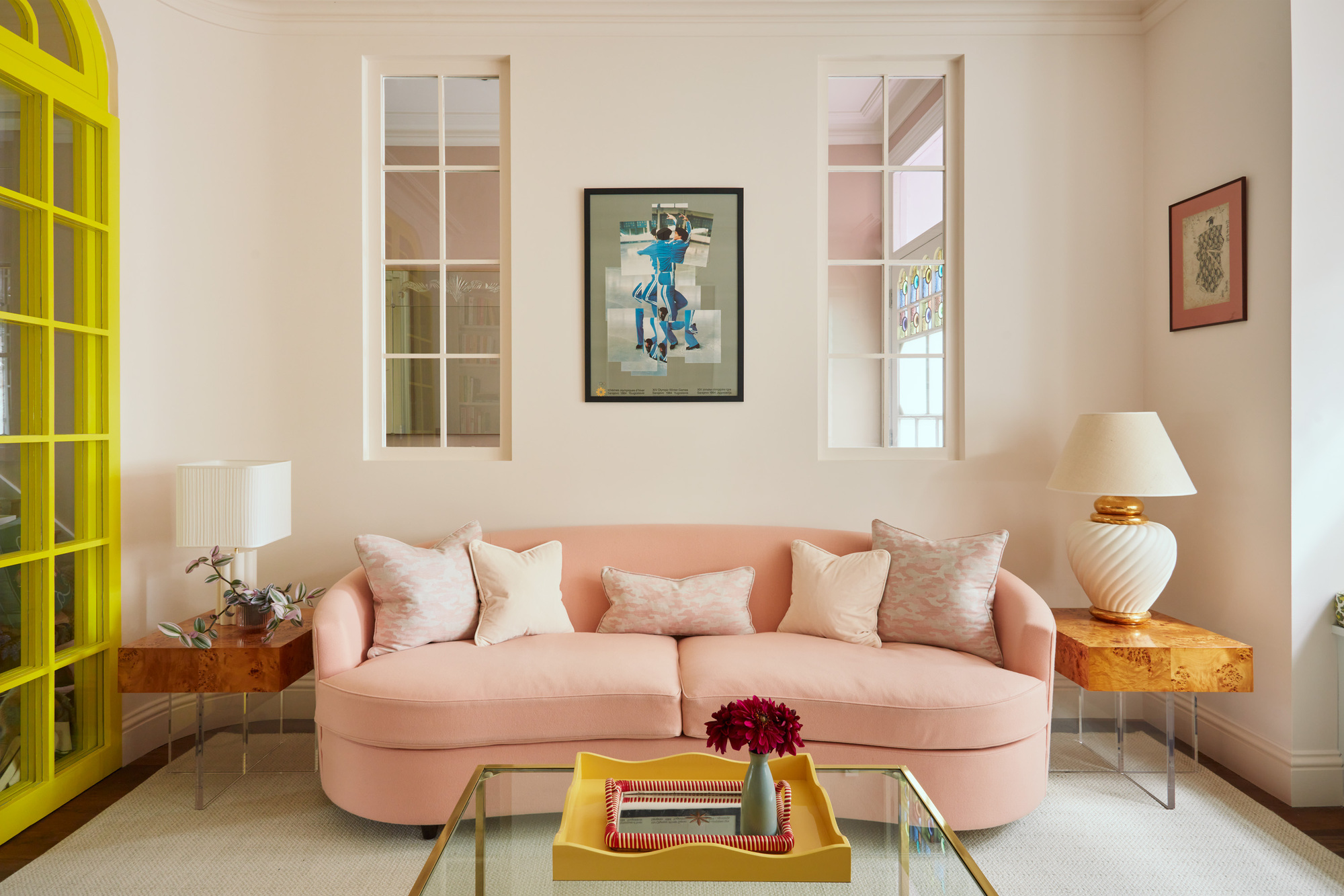 modern living room with pale pink curved sofa, glass coffee table with yellow tray, two side tables with lamps, bright yellow trim, with internal windows