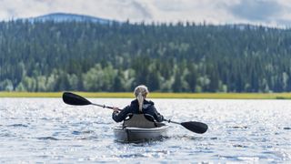 Woman kayaking along a lake looking out at the tree view