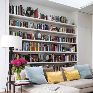 White living room with floor-to-ceiling bookshelves behind sofa