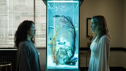 Eve and Villanelle stand opposite each other across a fish tank in season 4 of Killing Eve