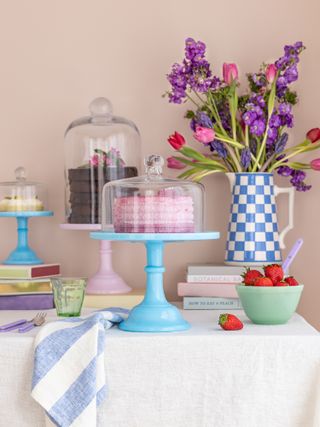 Table set with white tablecloth, blue and pink cake stands and blue and white checkered jug