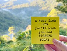 Someone holds a yellow sticky note saying "A year from now you'll wish you had started today!" There are mountains in the background.
