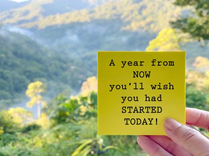 Someone holds a yellow sticky note saying "A year from now you'll wish you had started today!" There are mountains in the background.