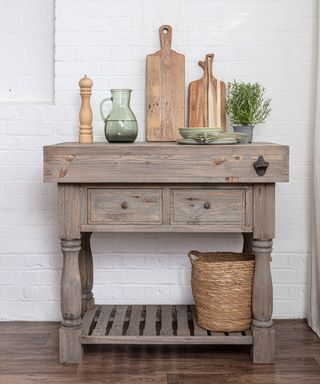 A reclaimed wood butcher's block kitchen island with light, grainy finish and a woven basket below it