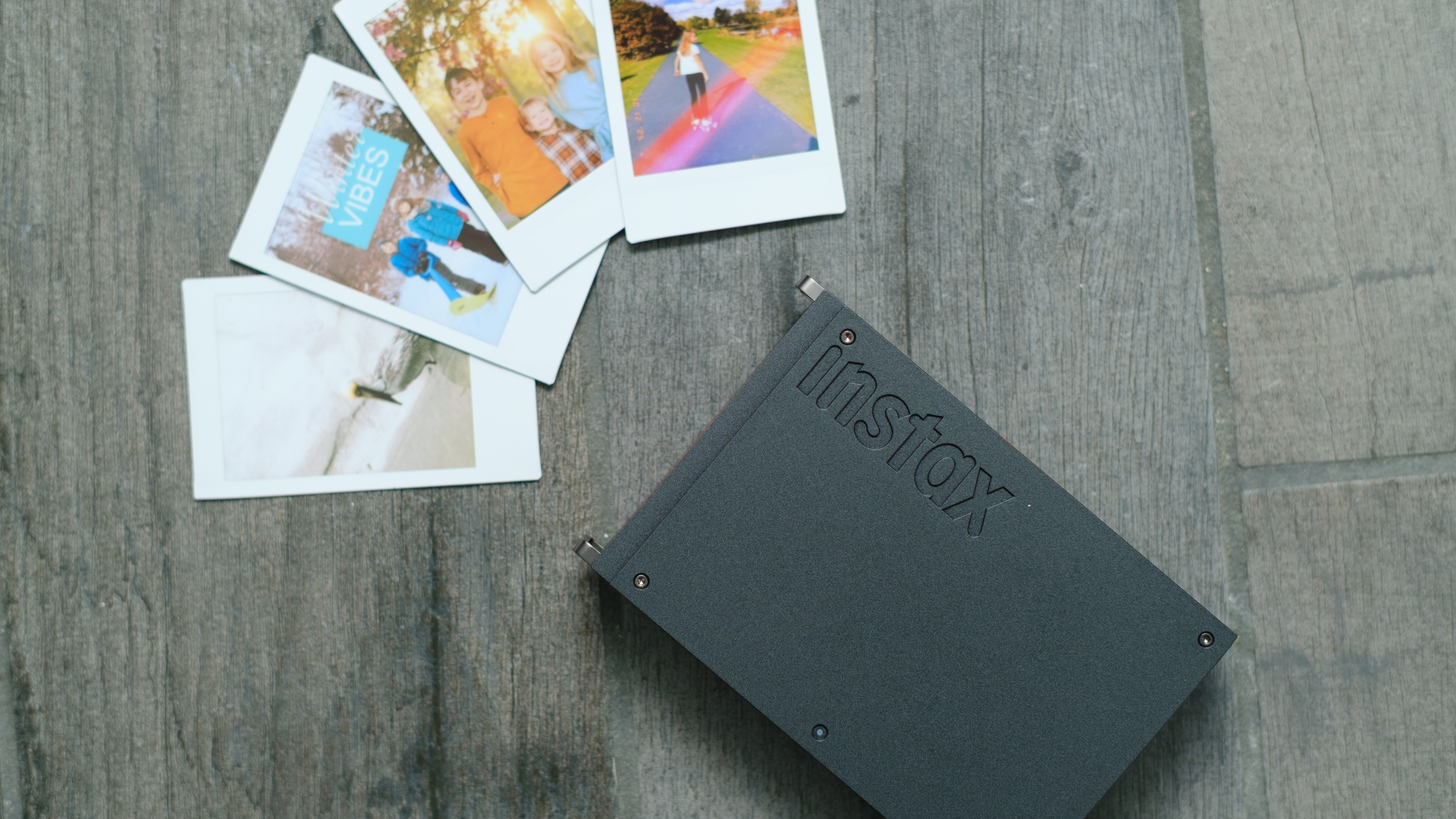 The Fujifilm Instax Mini Link+ on a gray background with instant prints