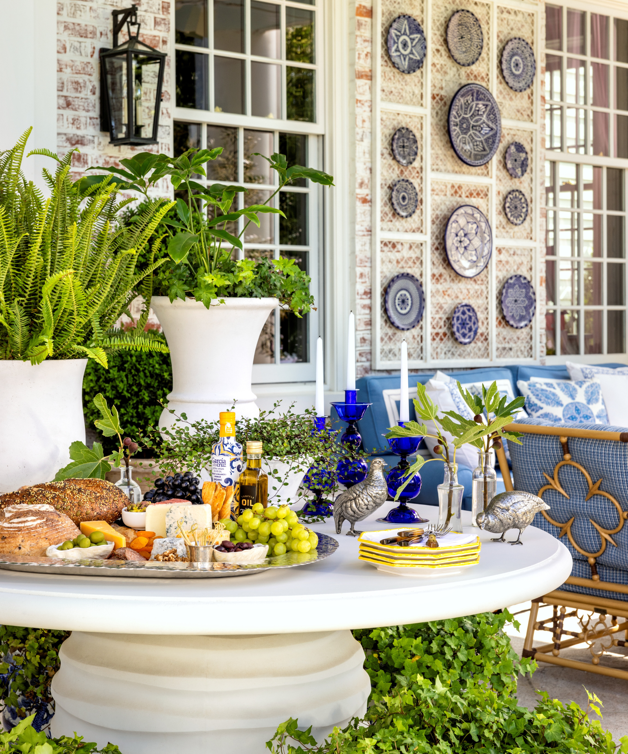 Outdoor pedestal dining table topped with a silver appetizer platter mingled with eclectic decorations