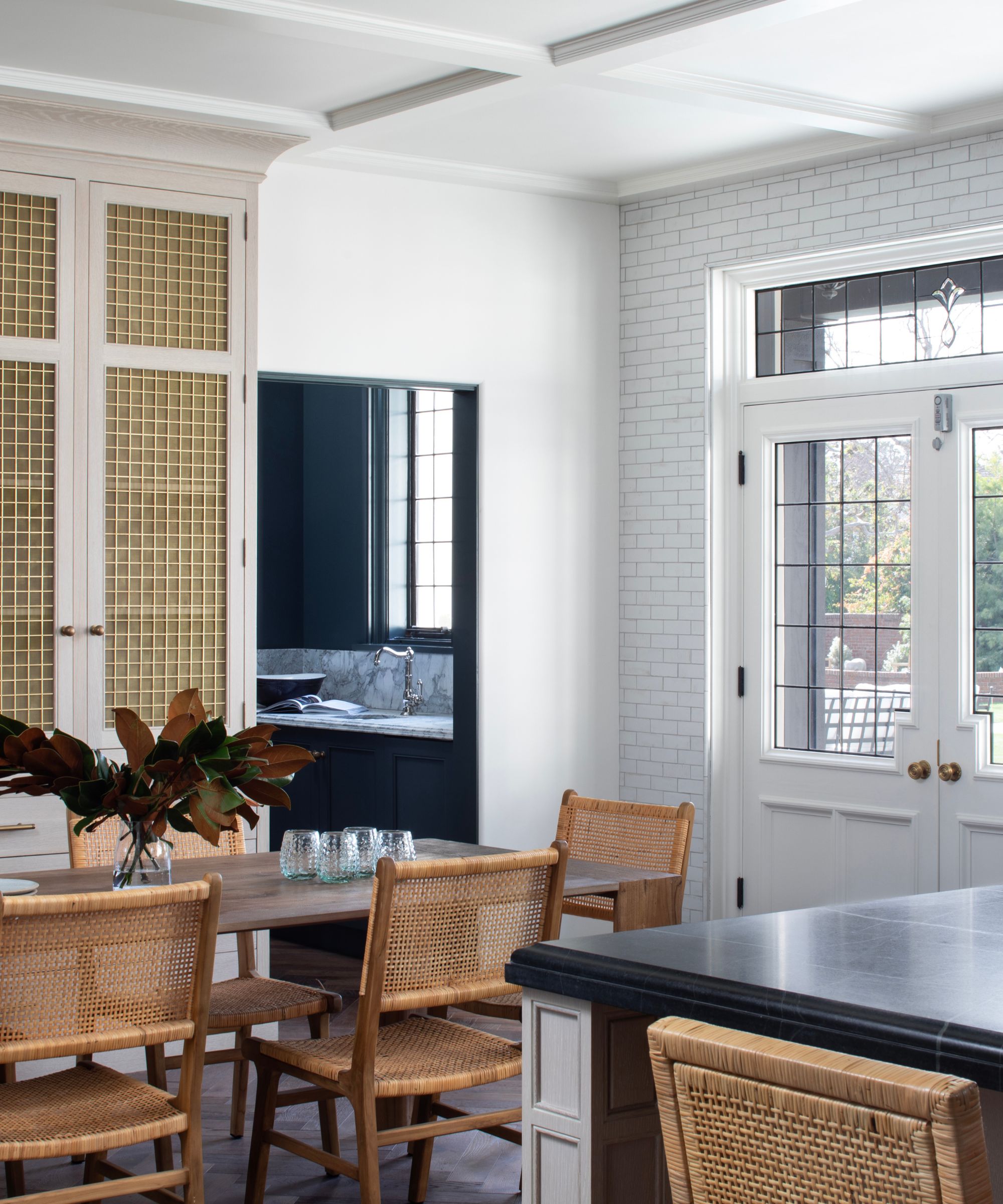 Dining area in an open plan kitchen with white walls and a wooden table with rattan chairs