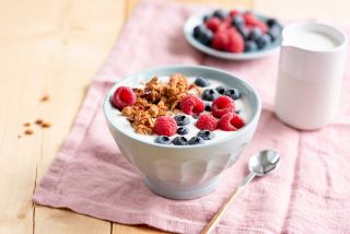 Yogurt with granola and berries in bowl on wooden table.