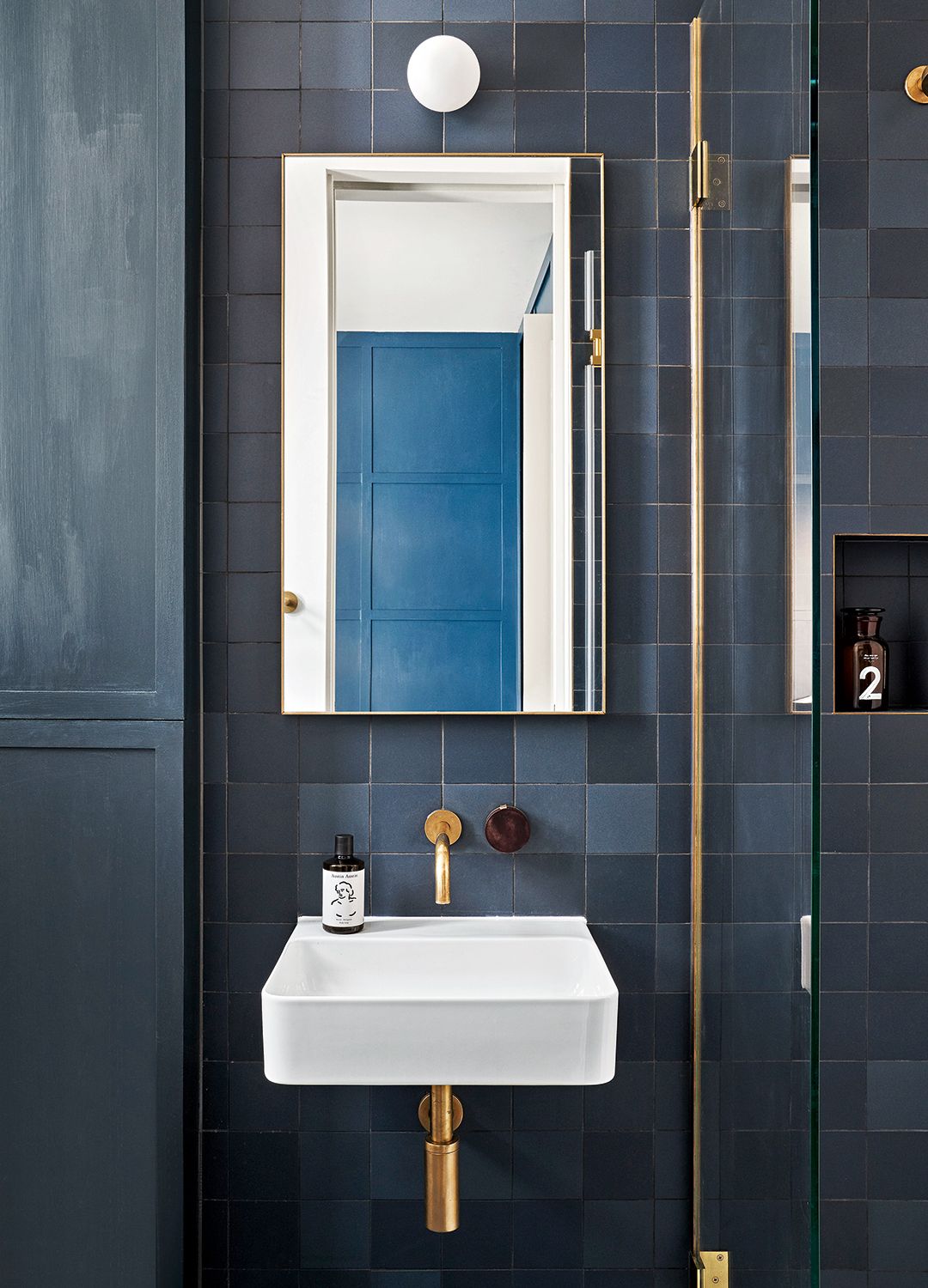 Dark blue tiled bathroom with gold taps and fittings with a small white square basin