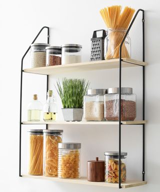 An image of black metal shelving unit with wooden shelves with jars or dried goods, potted herbs and oil bottles on them