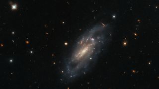 hubble photo of a spiral galaxy in deep space, with more distant galaxies in the background