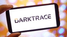 Darktrace logo and branding pictured on a smartphone screen held in a person's hand.