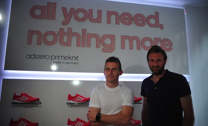 Two men standing in front of a display featuring red trainers and the words &quot;all you need, nothing more&quot;