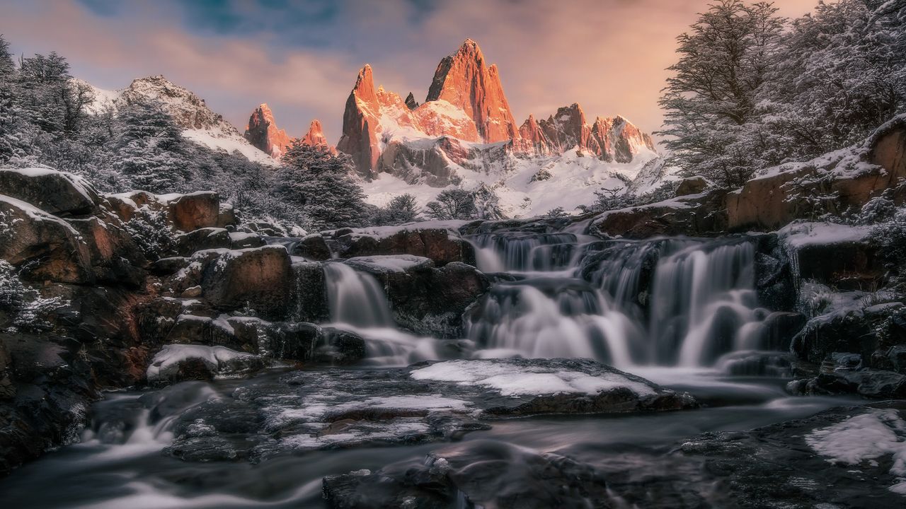 Shadowy waterfall in front of sunlit mountain.