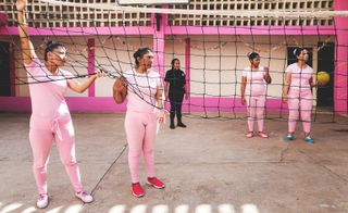 Women wearing pink, holding a volleyball net