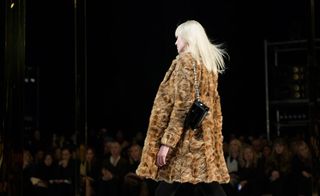 Catwalk model wearing a caramel-coloured fur coat and a small black leather bag