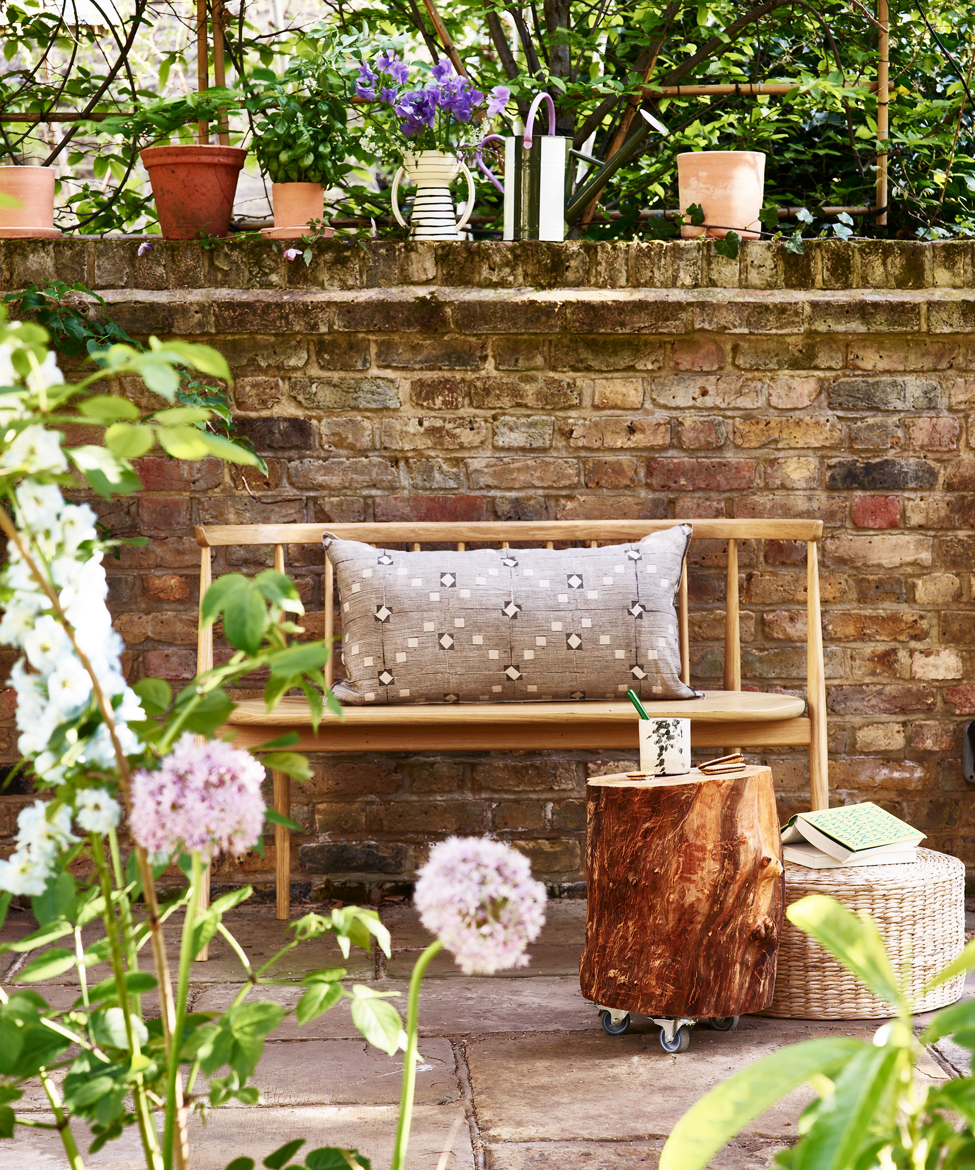 Wooden bench in front of garden wall with potted plants around a stump table