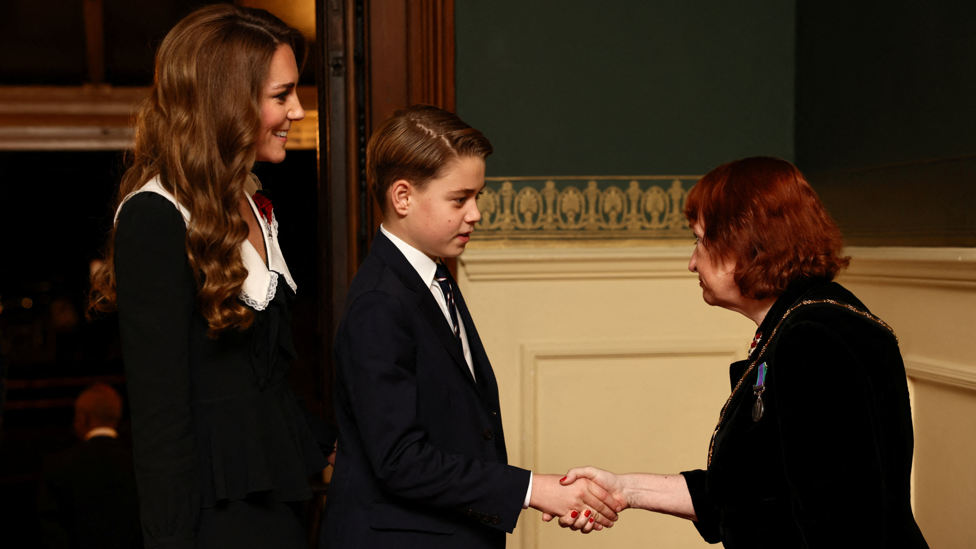 Prince George shaking hands with a woman with Princess Kate standing behind her 