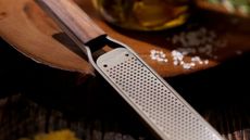 Microplane Master Series Wood Handle Zester Grater on a natural wood board next to a sprinkle of rock salt