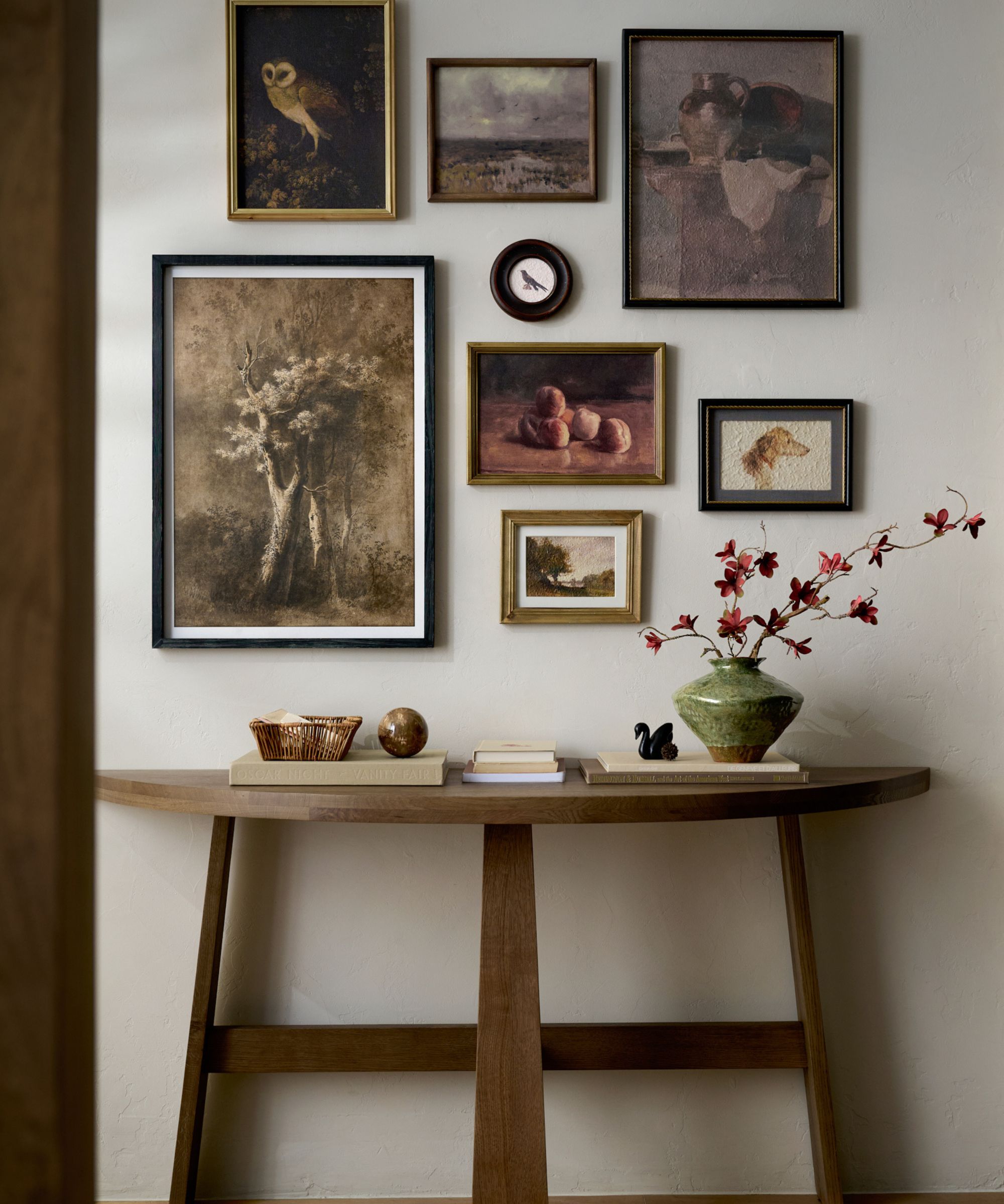 Hallway with wooden console with green vase and flowers, books and trinkets and gallery wall with vintage prints