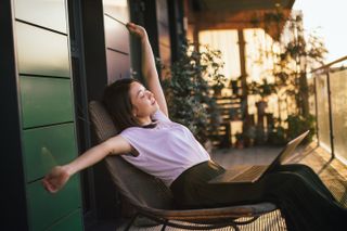 woman stretching whilst working on laptop outdoors on a balcony