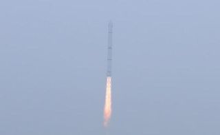 A Chinese Long March 4C rocket launches in a foggy blue sky.