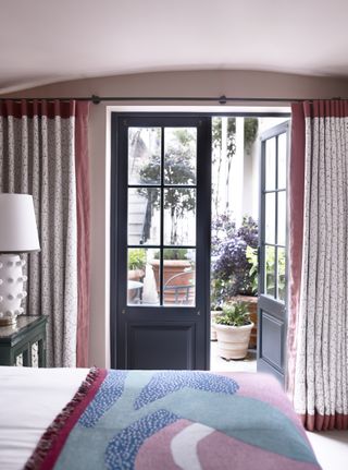 pink bedroom with painted French doors and curtains looking out into garden
