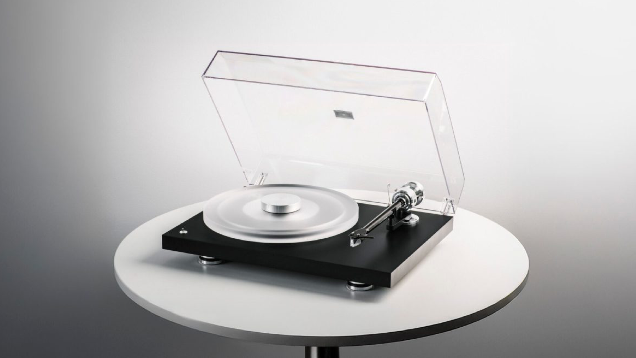 Pro-Ject Debut Reference 10 promotional image of the turntable sitting on a white circular table against a graded grey background