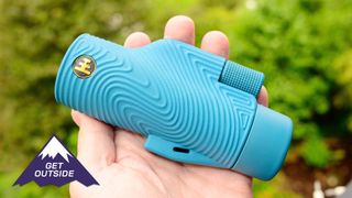 Nocs Field Tube Monocular in baby blue. Shown in a user's hand against a green background.