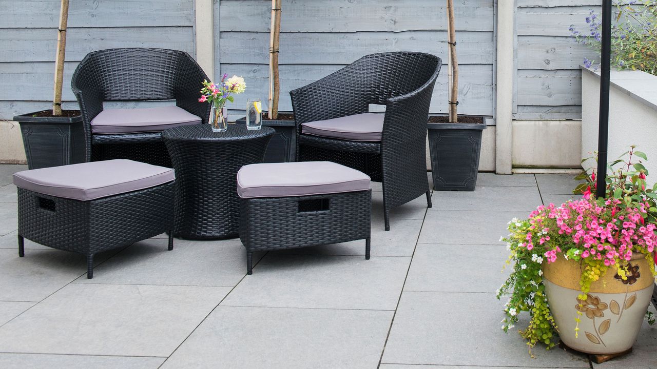 A redesigned low maintenance garden with hard landscape, Grey fencing and seats and a table, and a low wall and concrete patio