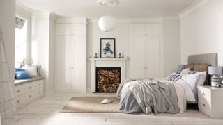 bedroom with white walls, built in alcove wardrobes to either side of fireplace stacked with logs and a built in window seat