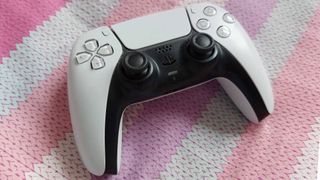 A DualSense controller is seen on a colourful background, with stripes of pink, purple, and blue.