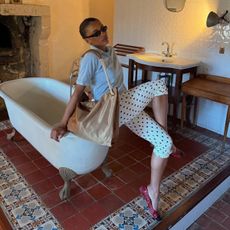 A woman sitting wearing polka dot capris, a gray polo, and a large gold tote. 