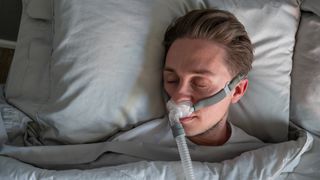 Close Up Of A Young Man With Sleep Apnea Wearing A CPAP Mask In Bed Sleeping On His Side