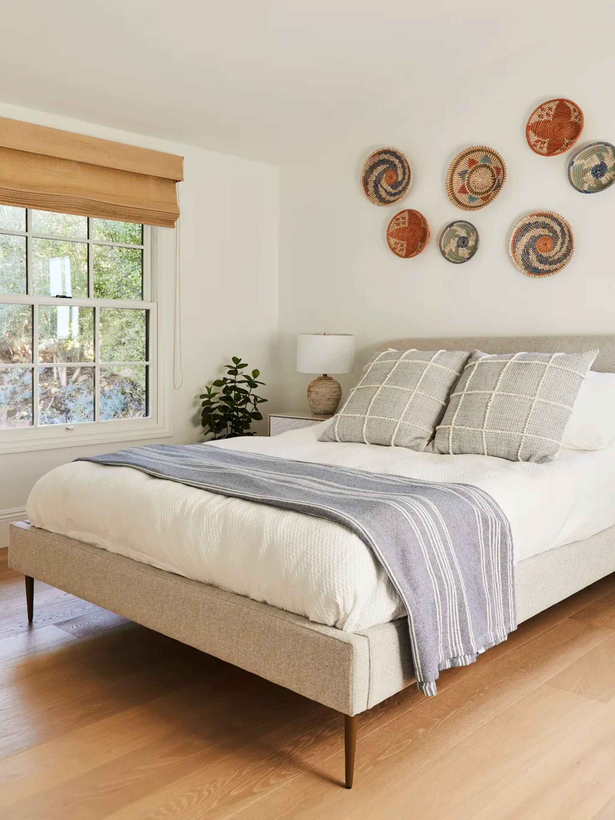 bedroom with a white bed and green checkered pillows as well as seven decorative bowls hanging on the wall