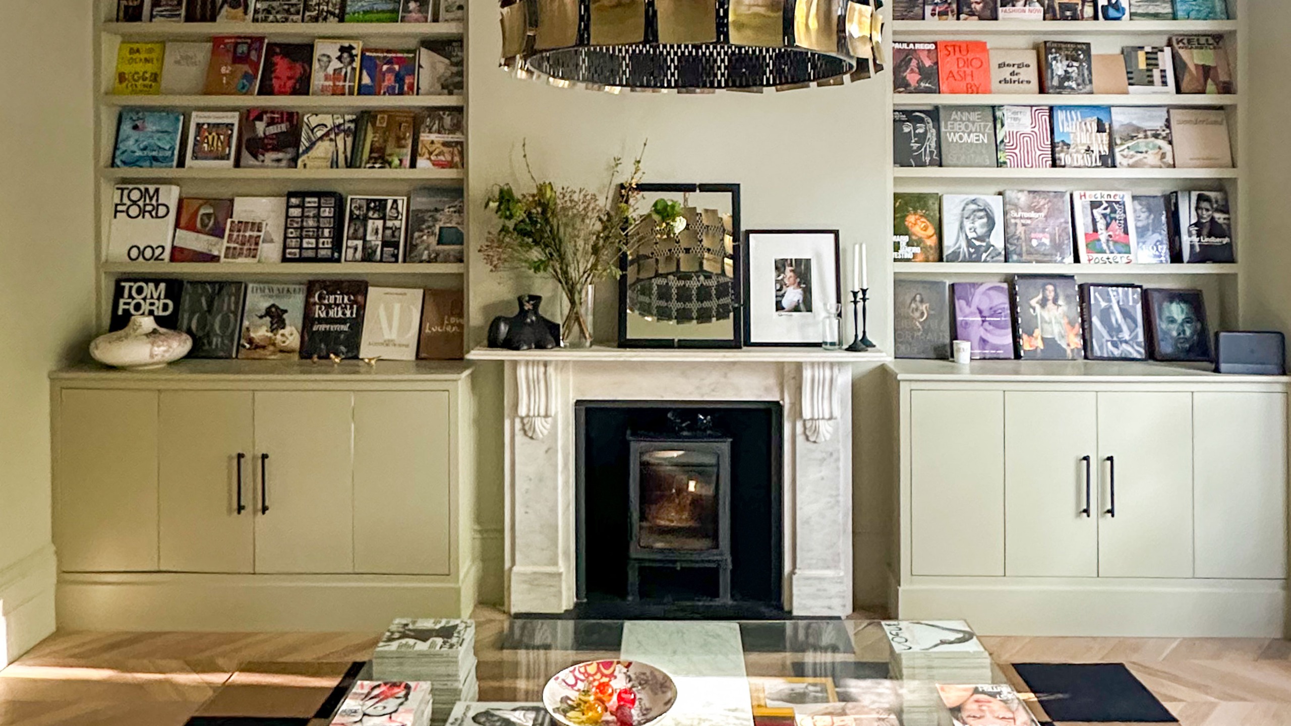 Living room with built in magazine display shelving above cupboards on either side of marble fireplace