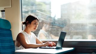 Young woman on a laptop on a train working, business and technology. 