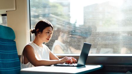 Young woman on a laptop on a train working, business and technology. 