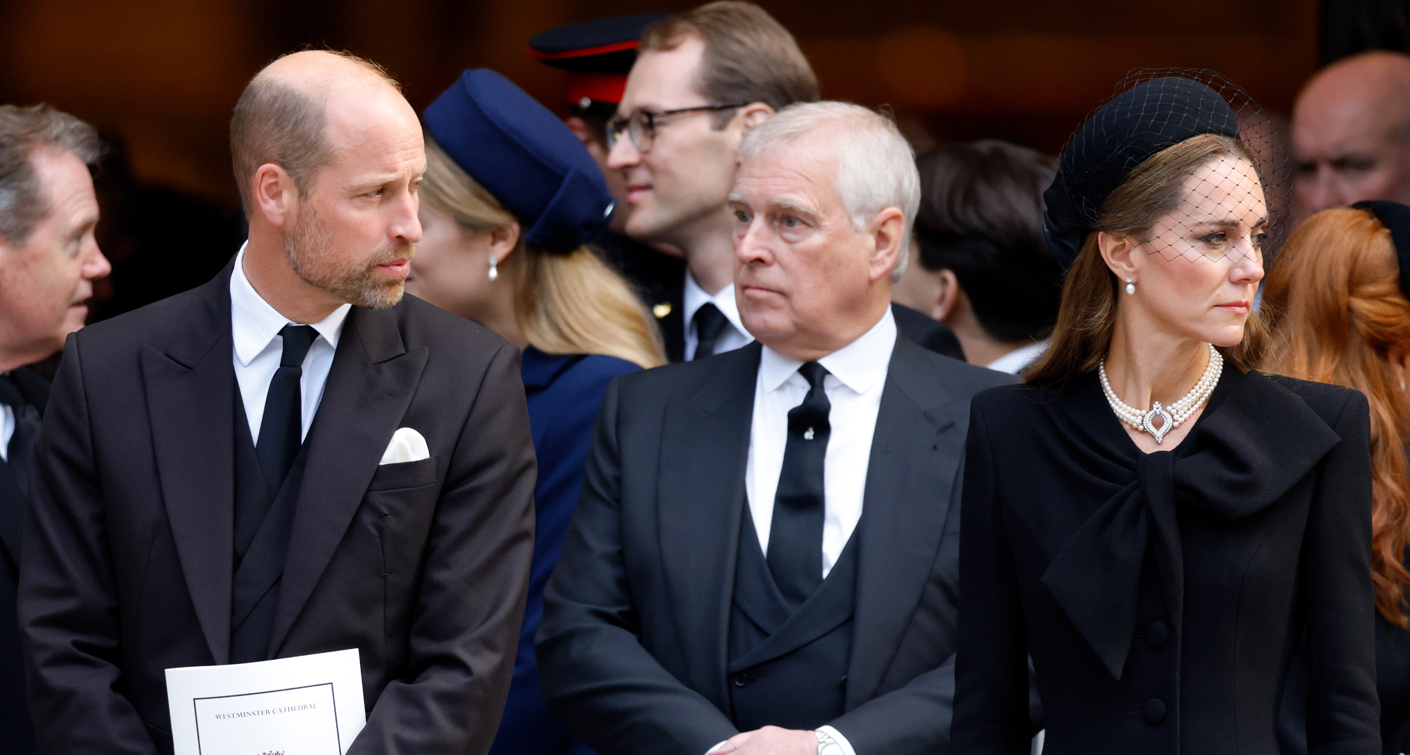 Prince Andrew, Prince William and Princess Kate standing in a row wearing black at a funeral