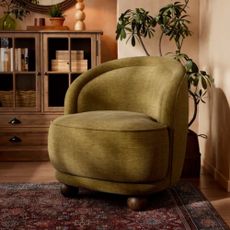Dunelm Chenille Ball Foot Tub Chair in green with wooden feet - on traditional-style rug with plant in background and wooden furniture