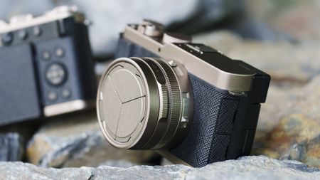 The Gold Titanium Special Edition of the Panasonic Lumix L10 compact camera, sat on gray and rust-colored rocks